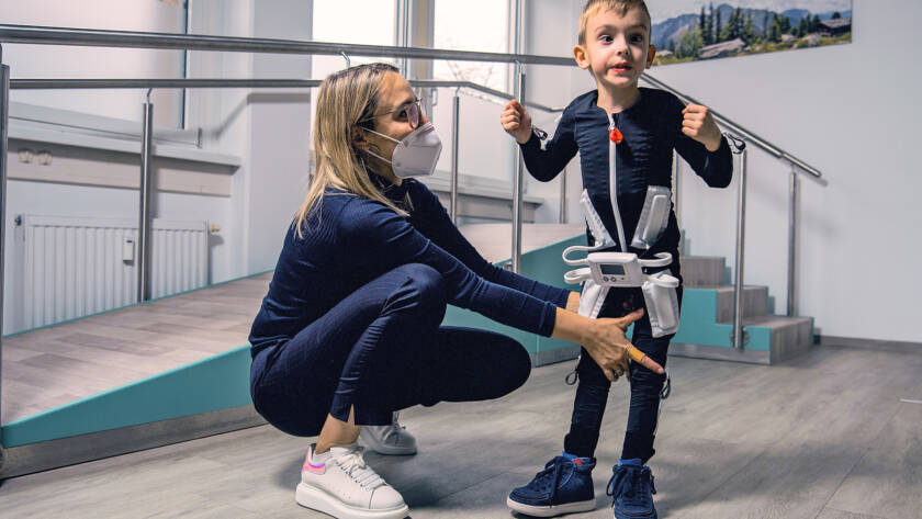 Criança com paralisia cerebral usando a Exopulse Mollii Suit durante sessão de reabilitação neurológica assistida