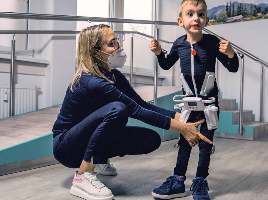 Criança com paralisia cerebral usando a Exopulse Mollii Suit durante sessão de reabilitação neurológica assistida